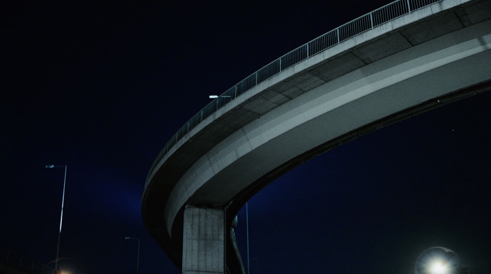 Reference film still: the underside of a curved flyover at night